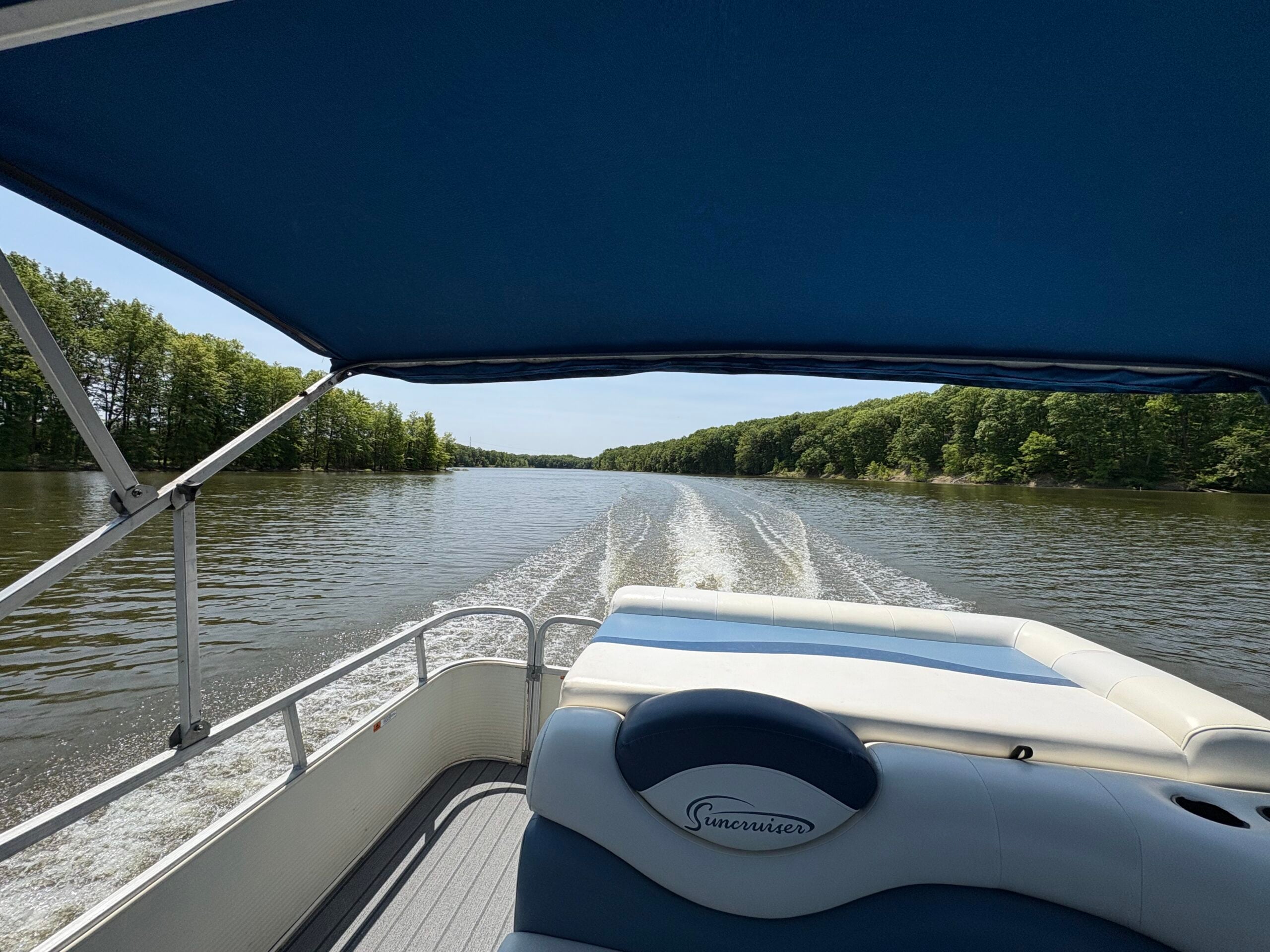 The view of Berlin Lake from the back side of a pontoon boat. The water looks peaceful, and a blue bimini top provides shade on the boat.