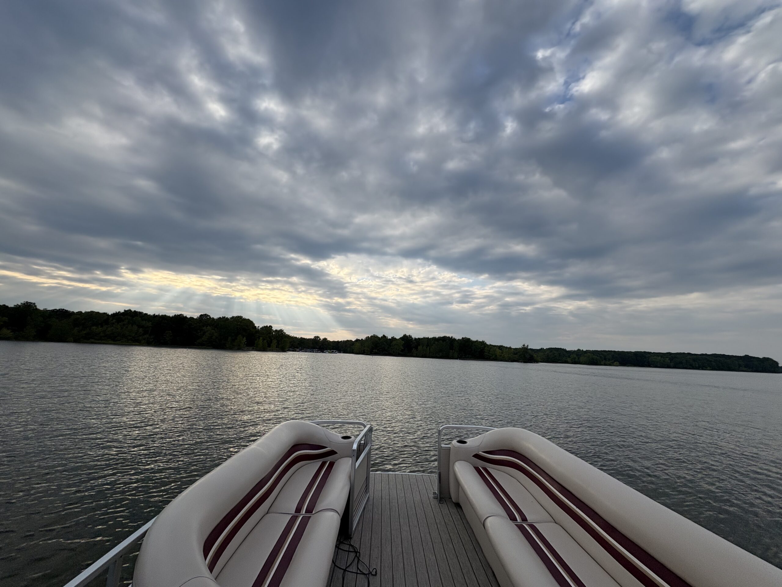 The view of Berlin Lake from the back side of a pontoon boat. The water looks peaceful, and a blue bimini top provides shade on the boat.